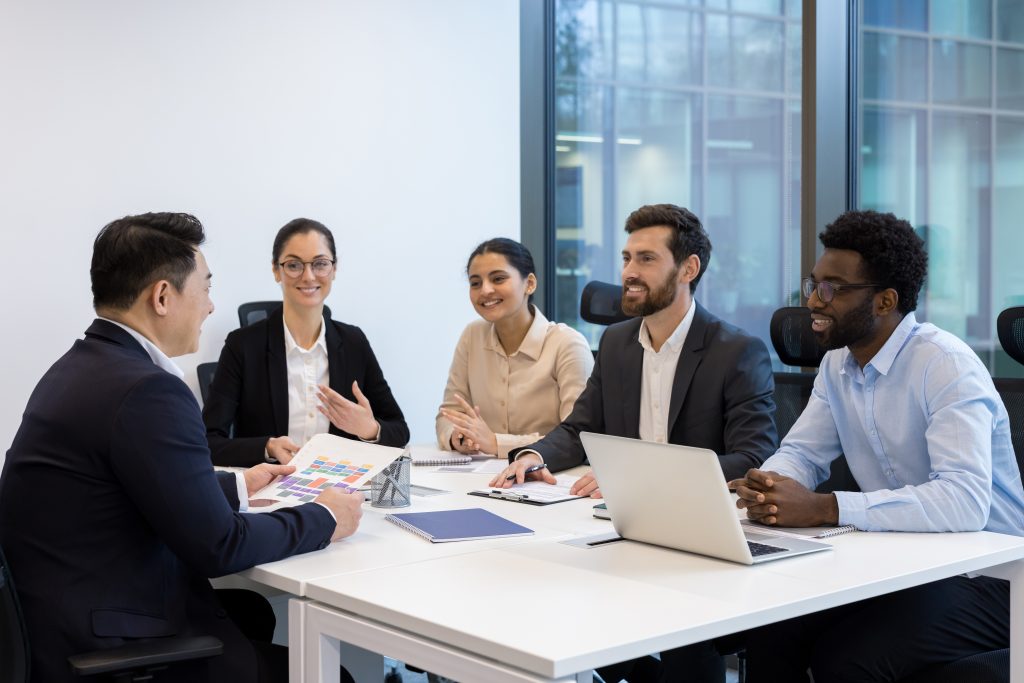Diverse business meeting of colleagues, people sitting at table in conference room inside company office, discussing business project and new startups.