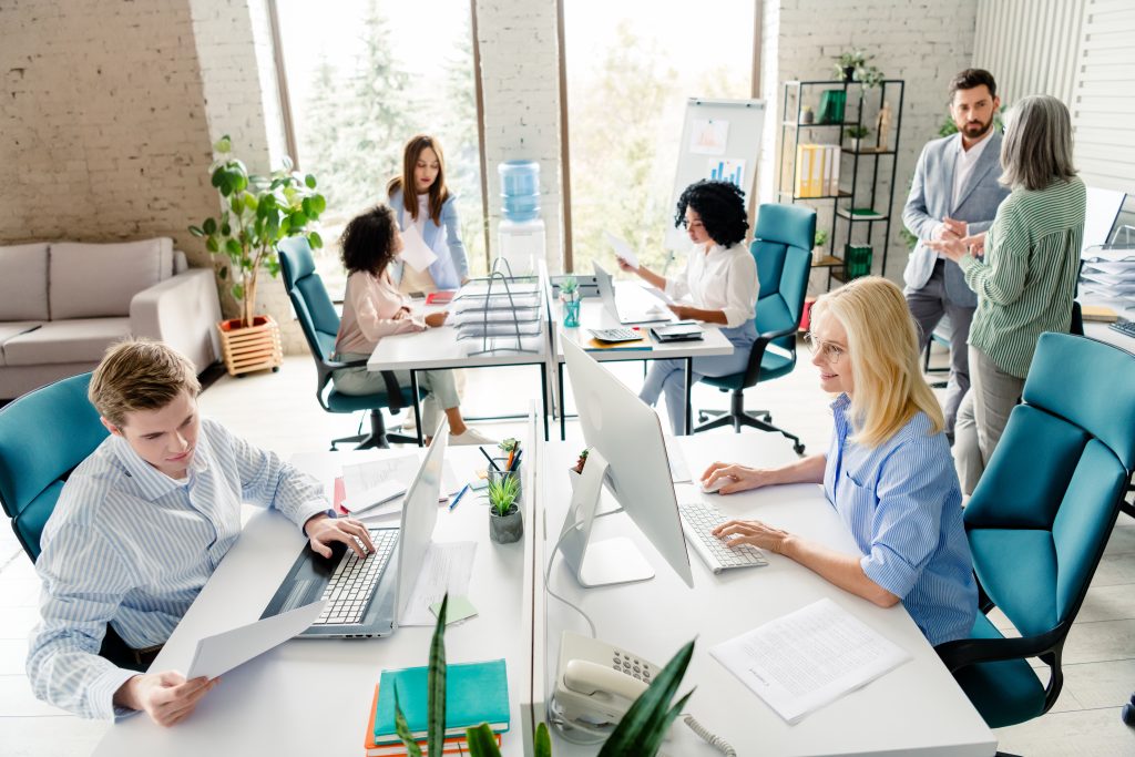 Group of employees working in a contemporary office environment while engaging in teamwork, collaboration, and individual tasks under natural light in an organized and professional workspace.