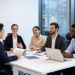 Diverse business meeting of colleagues, people sitting at table in conference room inside company office, discussing business project and new startups.