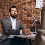 Businessman analyzing renewable energy project with miniature wind turbine model in the foreground, discussing with a colleague