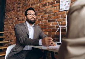 Businessman analyzing renewable energy project with miniature wind turbine model in the foreground, discussing with a colleague