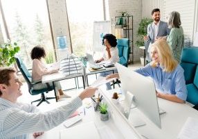 Diverse team members working collaboratively in a brightly lit office space, showcasing teamwork and professional interaction amidst a modern workspace.