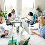 A busy office filled with professionals collaborating, working, and discussing projects, emphasizing teamwork and productivity in a stylish and well-lit environment.