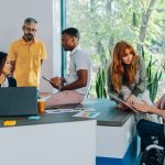 Multicultural team having meeting and briefing at boardroom and analyzing charts and documents. Inclusive colleagues discussing documents and paperwork with a businesswoman who uses a wheelchair.