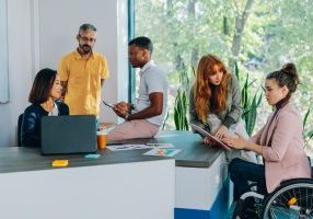 Multicultural team having meeting and briefing at boardroom and analyzing charts and documents. Inclusive colleagues discussing documents and paperwork with a businesswoman who uses a wheelchair.