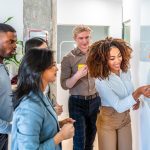 Group of young businesspeople sharing ideas in the office during a productive meeting, using colorful sticky notes on a whiteboard