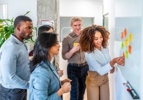 Group of young businesspeople sharing ideas in the office during a productive meeting, using colorful sticky notes on a whiteboard