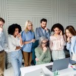 Colleagues gather around a laptop in an office, showing concentration and teamwork during a collaborative business session, illustrating professionalism and workplace collaboration.