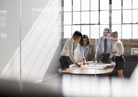 Four business colleagues stand talking in a meeting room