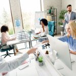 Diverse team members working collaboratively in a brightly lit office space, showcasing teamwork and professional interaction amidst a modern workspace.