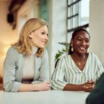 Two women discussing business matters while smiling, with a man present in the scene.